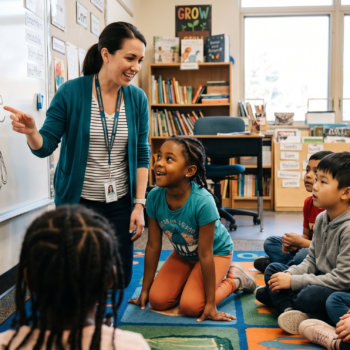 Teacher pointing to the word "reusable" on a whiteboard while students seated on a carpet engage in a base words lesson in an elementary classroom