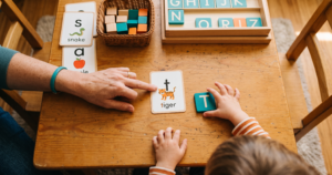 An adult points to a letter-sound flashcard during explicit phonics instruction as a young child matches the letter tile.