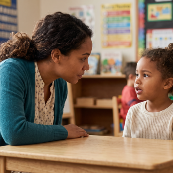 Teacher leaning in close to work on phoneme manipulation with a young student during a one-on-one oral language activity in an early childhood classroom