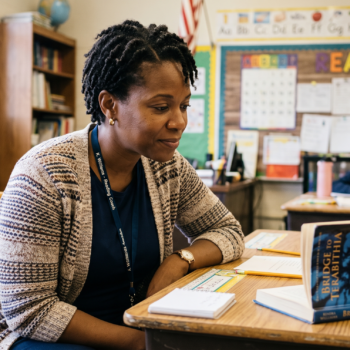 Reading coach listening attentively as a student reads aloud from Bridge to Terabithia during a one-on-one reading fluency session in an elementary classroom